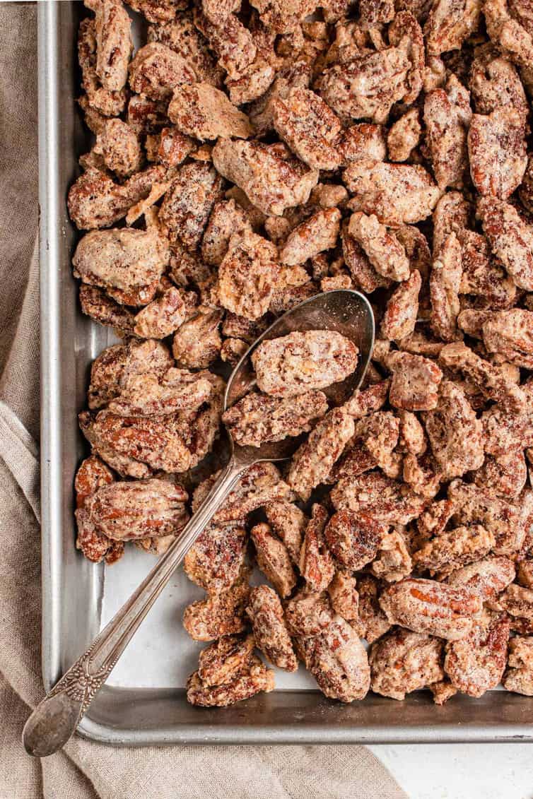A silver baking sheet with candied pecans and a silver spoon with a few pecans on the spoon.
