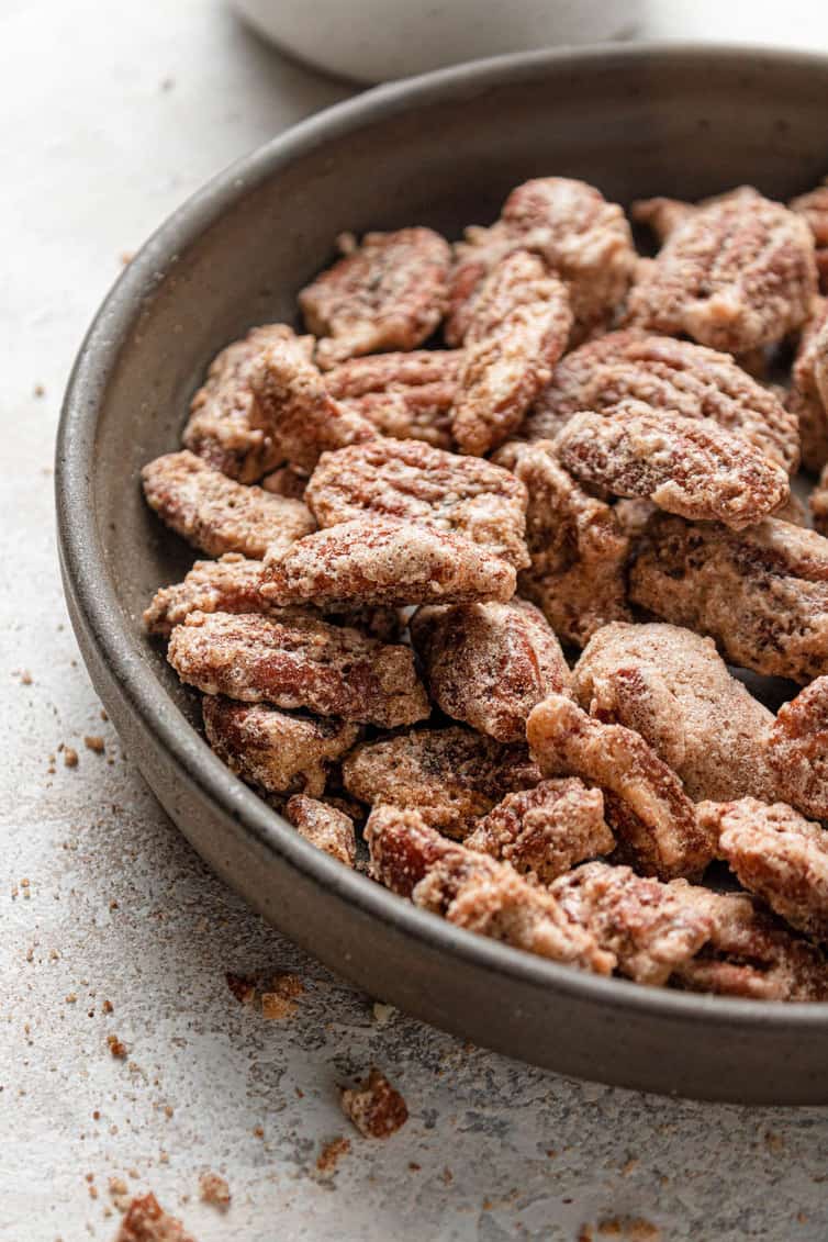 The left half of a brown bowl with cinnamon sugar candied pecans on a white counter.