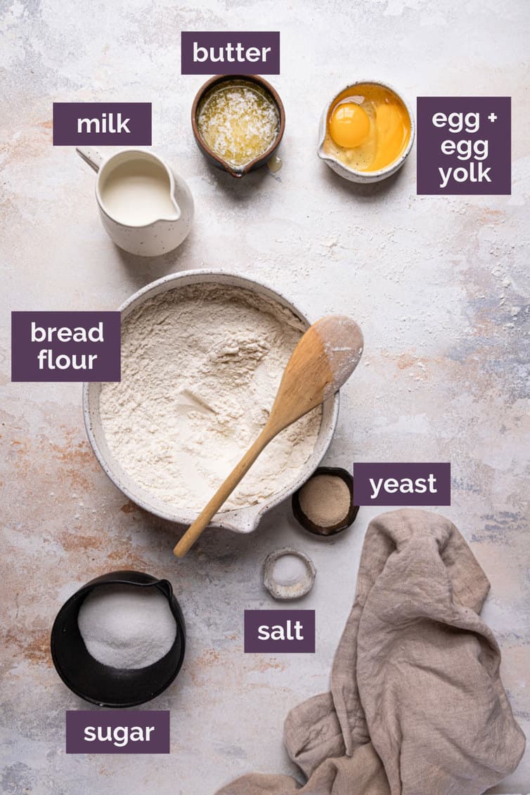 Ingredients for cinnamon rolls in bowls on a counter labeled with purple boxes.