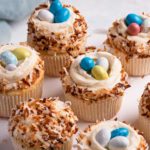 A square photo of coconut cupcakes topped with coconut frosting and toasted coconut.