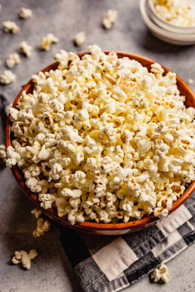 A brown bowl of popcorn on a black and white buffalo check towel with popcorn seasoning in the top left of the photo.