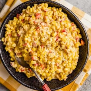 A square photo of Mexican corn salad in a black bowl on a white and yellow towel.