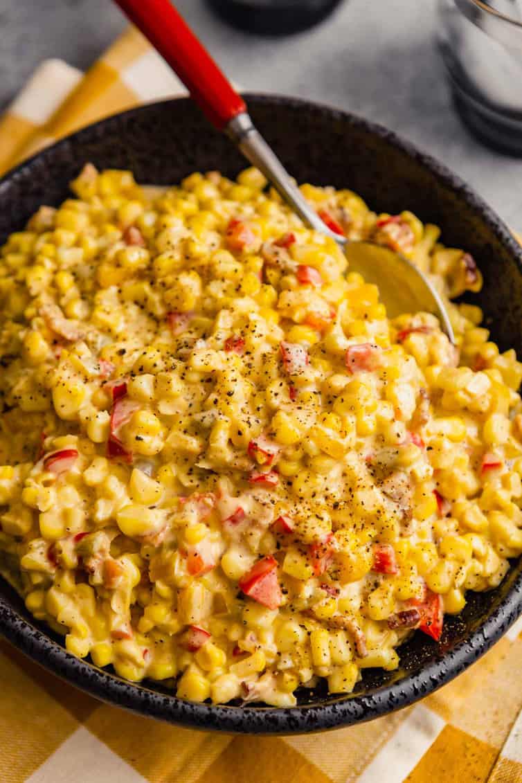 A black bowl on a white and yellow towel filled with easy Mexican corn salad and a silver spoon at the top with a red handle.