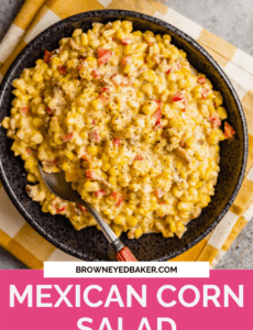 A black bowl of Mexican Corn salad with a spoon on a yellow and white towel with a pink rectangle at the bottom that says Mexican Corn Salad.