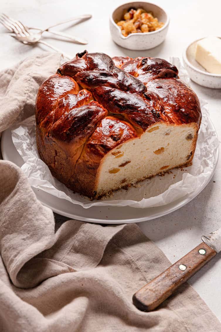 A loaf of paska bread with one slice take out on the left side with a knife on the left counter.