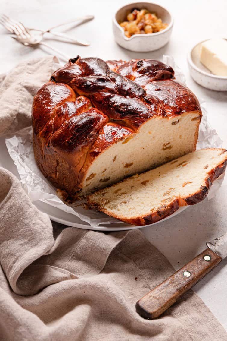 A loaf of paska bread on a parchment paper lined plate with a slice on the right side and a towel on the left side.