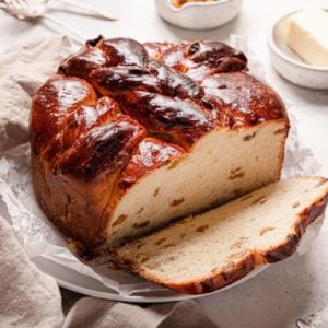 A square photo of a loaf of paska bread on a parchment paper with a slice in the front right.