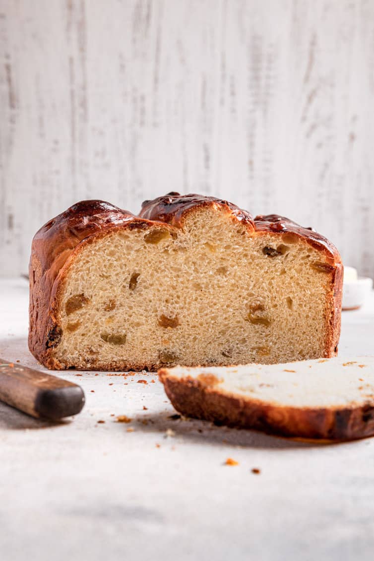 A tall loaf of paska bread with a slice cut down the front and the missing slice laying on it's side to the right.