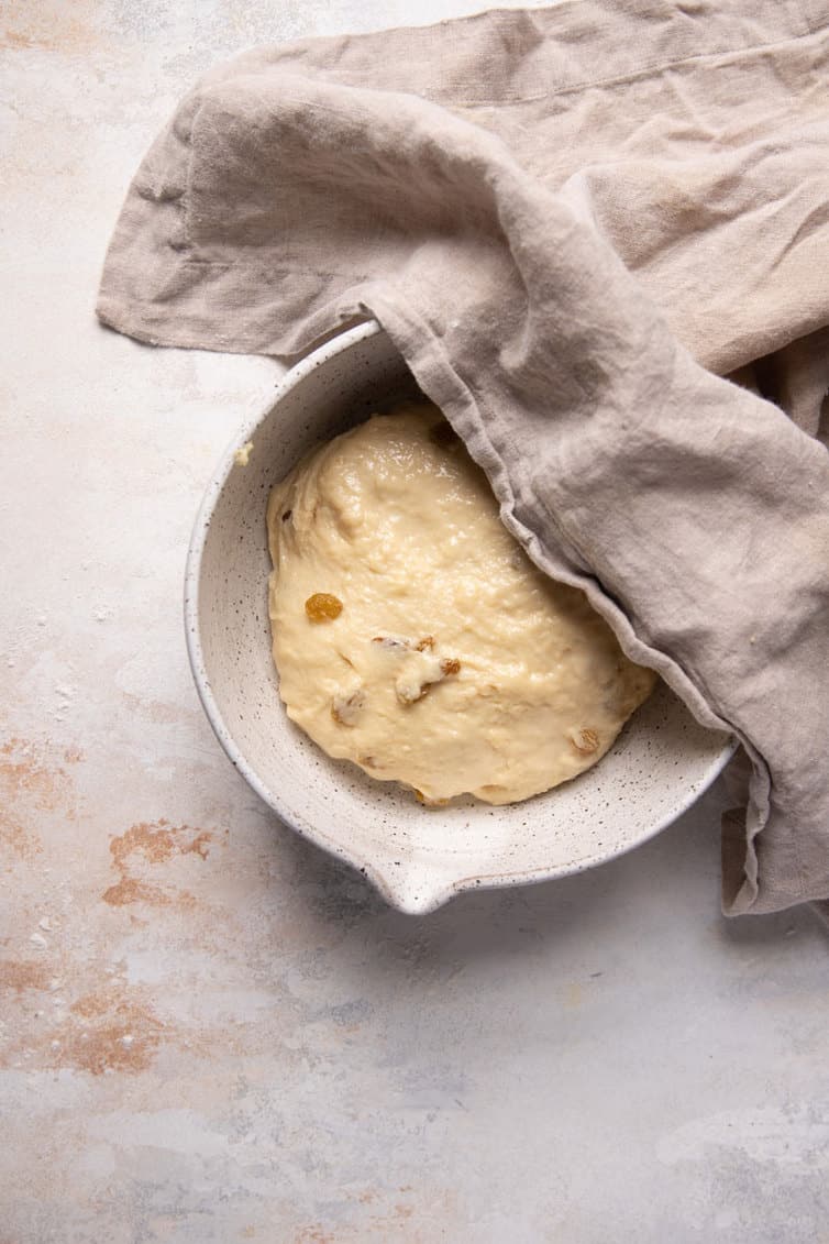 Paska bread dough rising in a bowl with a towel over the top left corner.