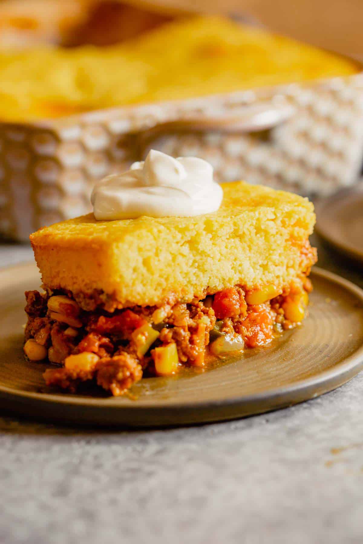 A brown plate topped with a serving of tamale pie in front of a casserole dish.