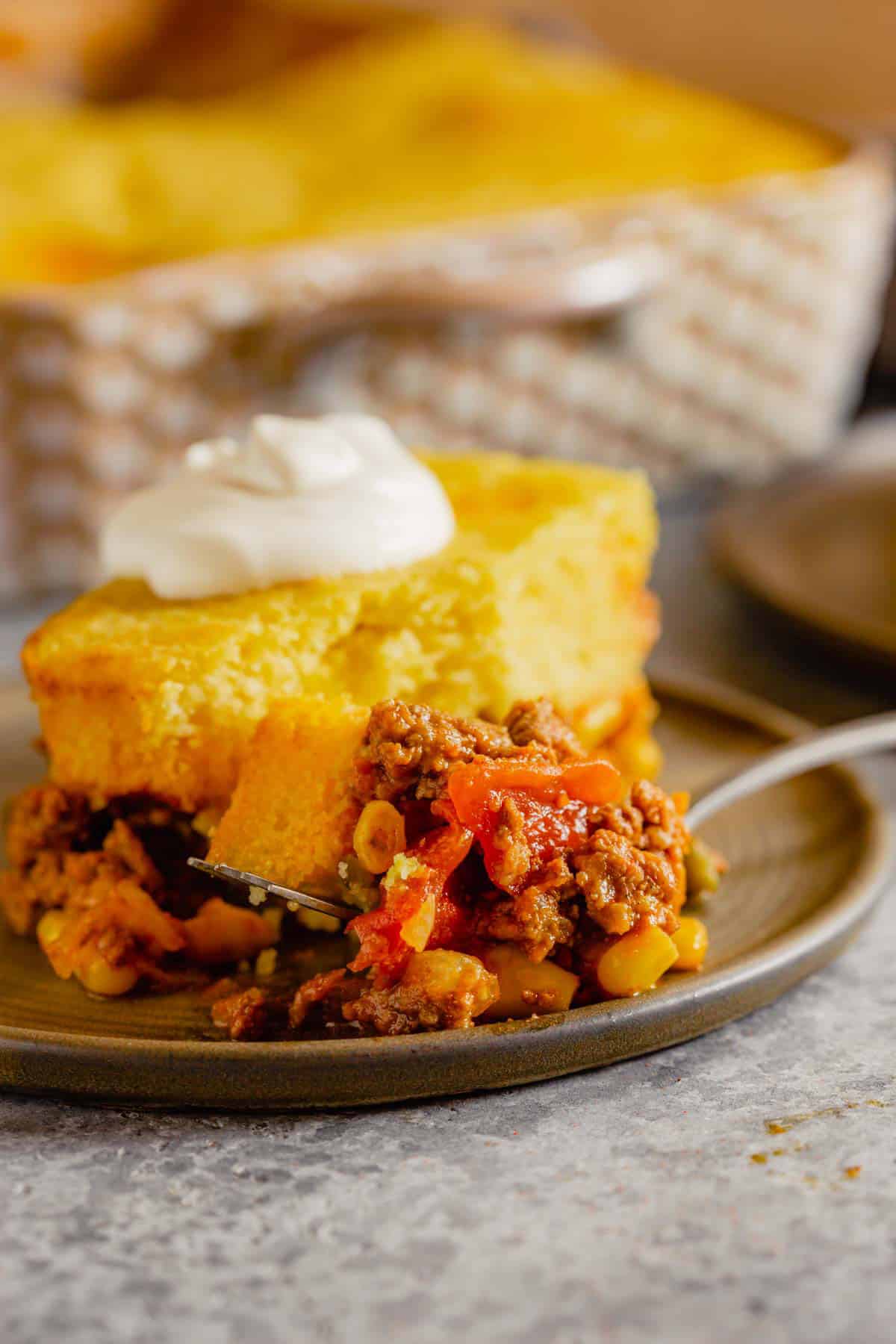A piece of tamale pie on a brown plate with a fork topped with tamale pie.