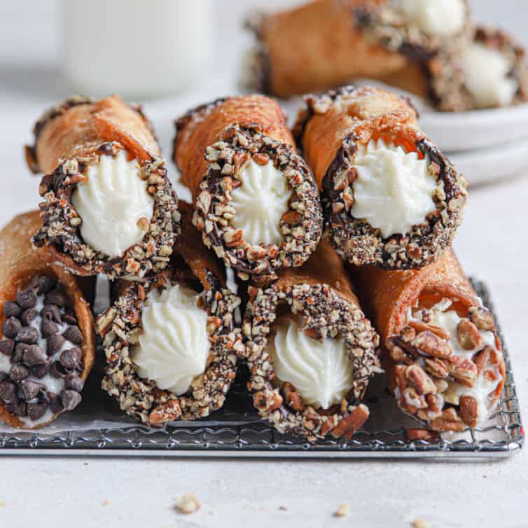 Two rows of homemade cannoli stacked on each other on top of a cooling rack.