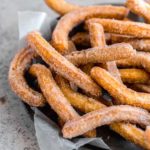 A pie pan lined with parchment paper and topped with fresh fried churros.
