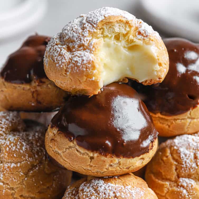A close up of the top of a tower of cream puffs that has one cream puff on top with a missing bite.