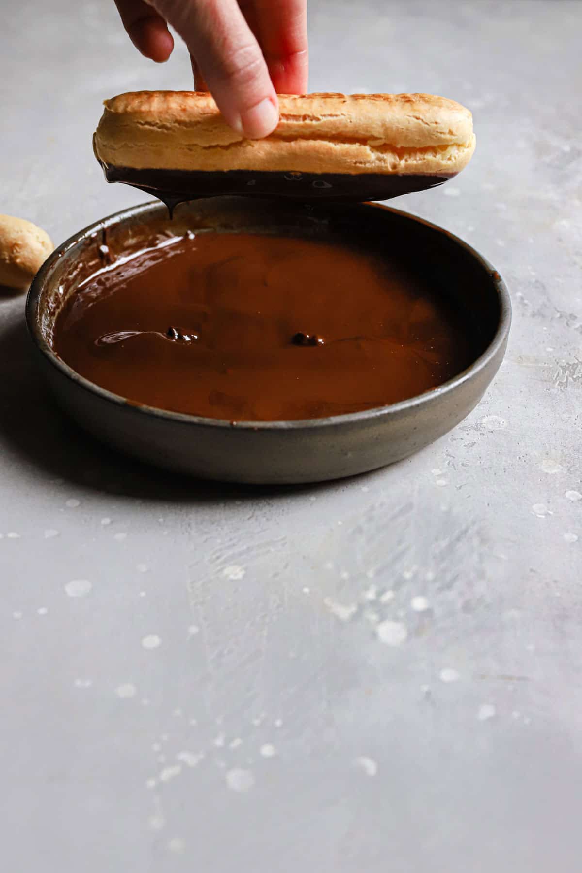 A hand holding an eclair upside down to dip it in the chocolate glaze.