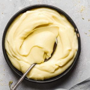 Top down photo of a black bowl with pastry cream and a silver spoon scooping pastry cream in the bowl.