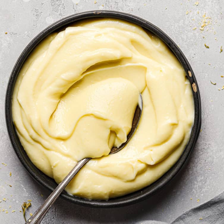 Top down photo of a black bowl with pastry cream and a silver spoon scooping pastry cream in the bowl.