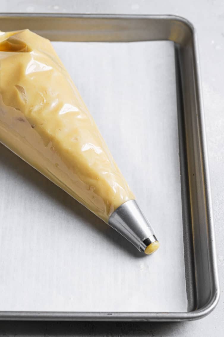 Pastry bag fitted with a round pastry tip and filled with choux pastry dough.