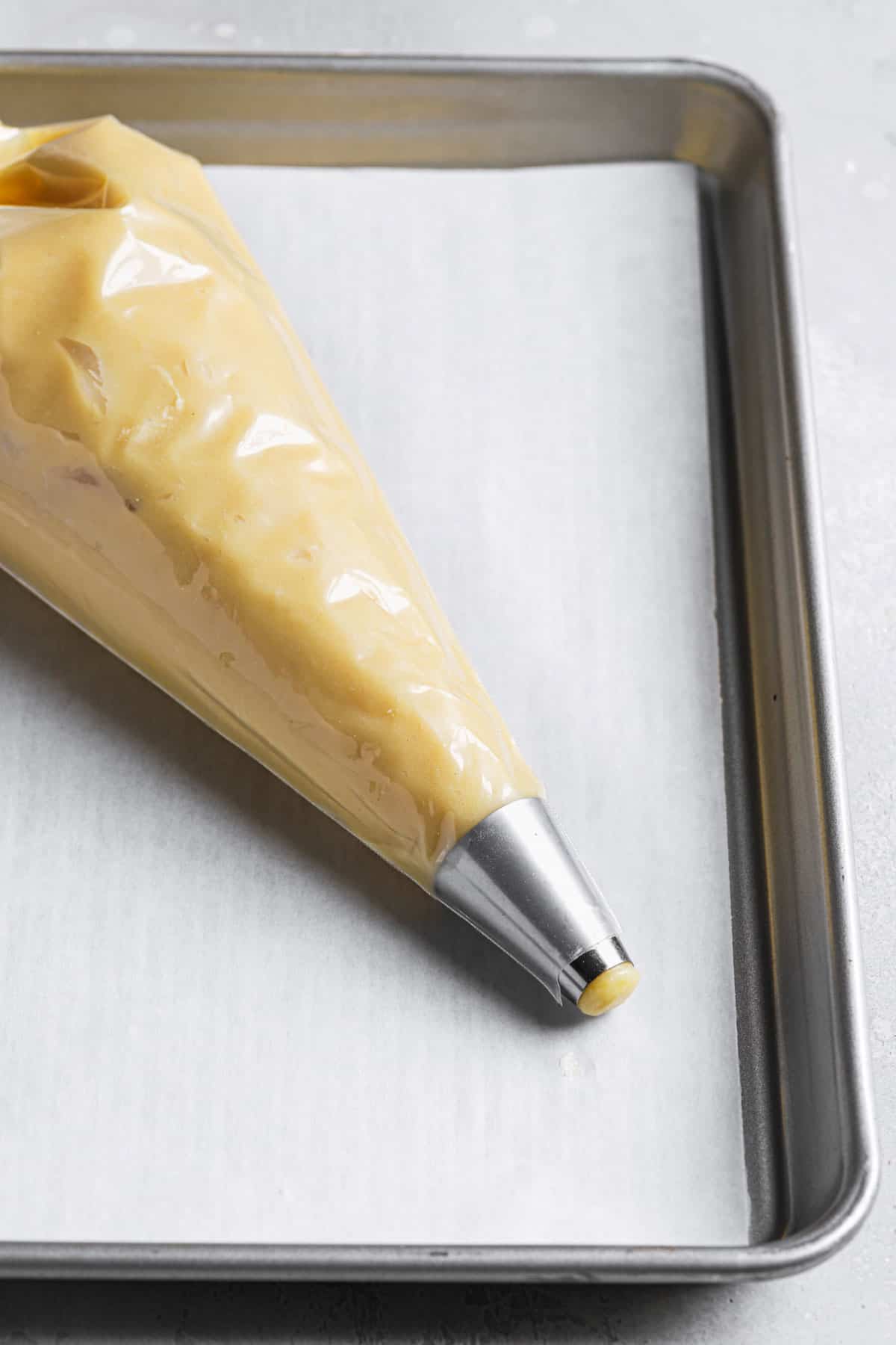 Pastry bag fitted with a round pastry tip and filled with choux pastry dough.