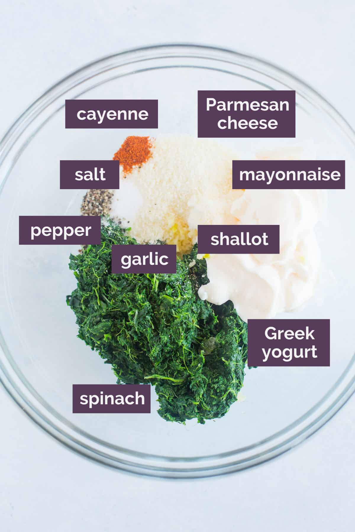 Ingredients for spinach dip in a glass bowl with purple labels naming the ingredeints.