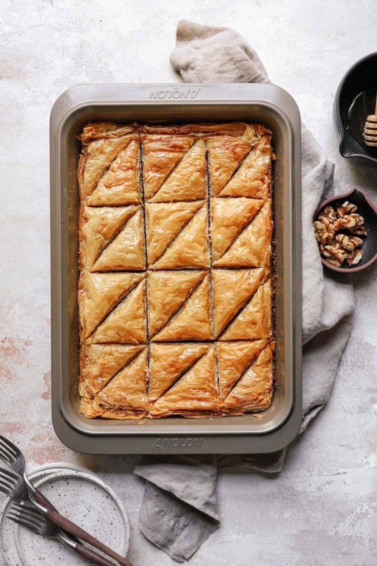 A top down photo of baklava on a counter with a dish towel and a small bowl of walnuts to the right.