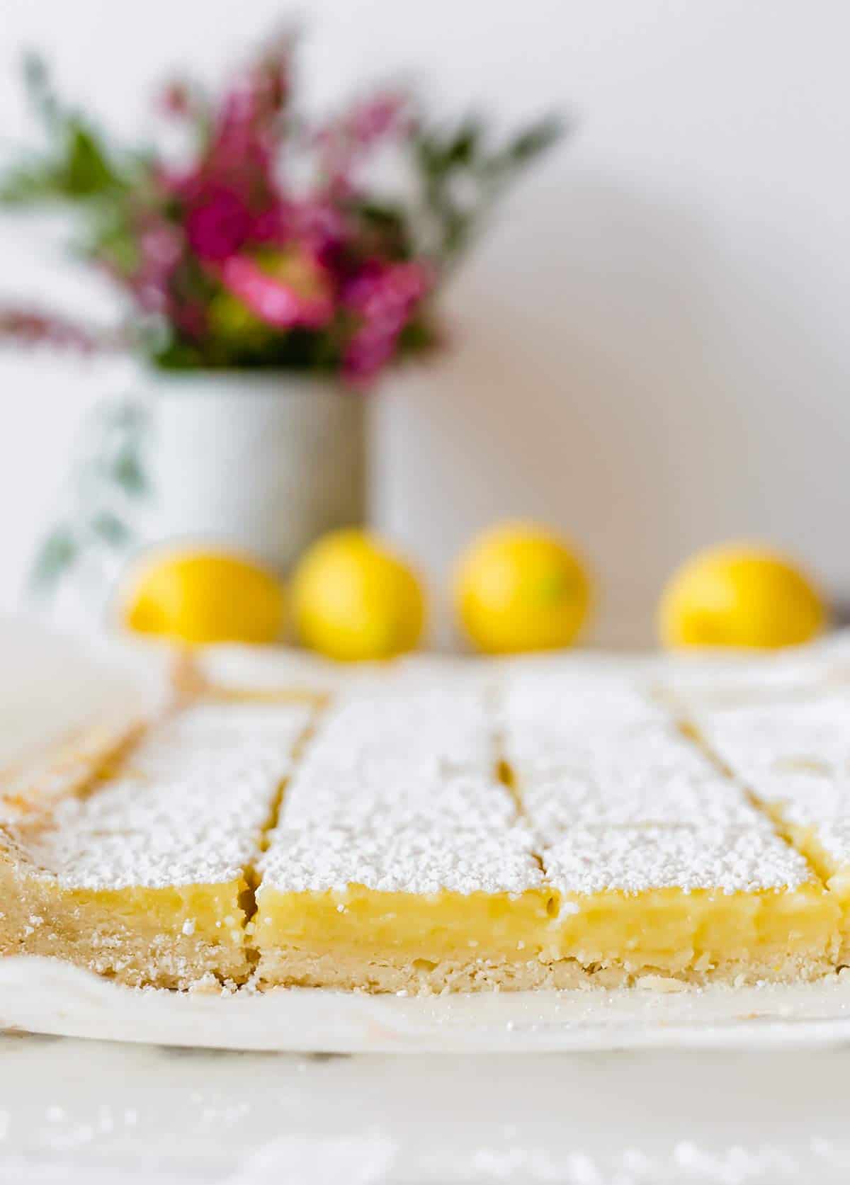 Lemon bars sliced into squares on a piece of parchment paper.