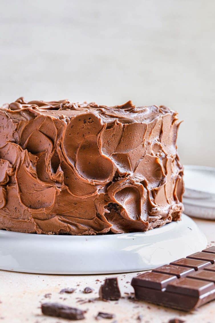 A full chocolate cake coated in chocolate frosting with a chocolate bar to the bottom right.