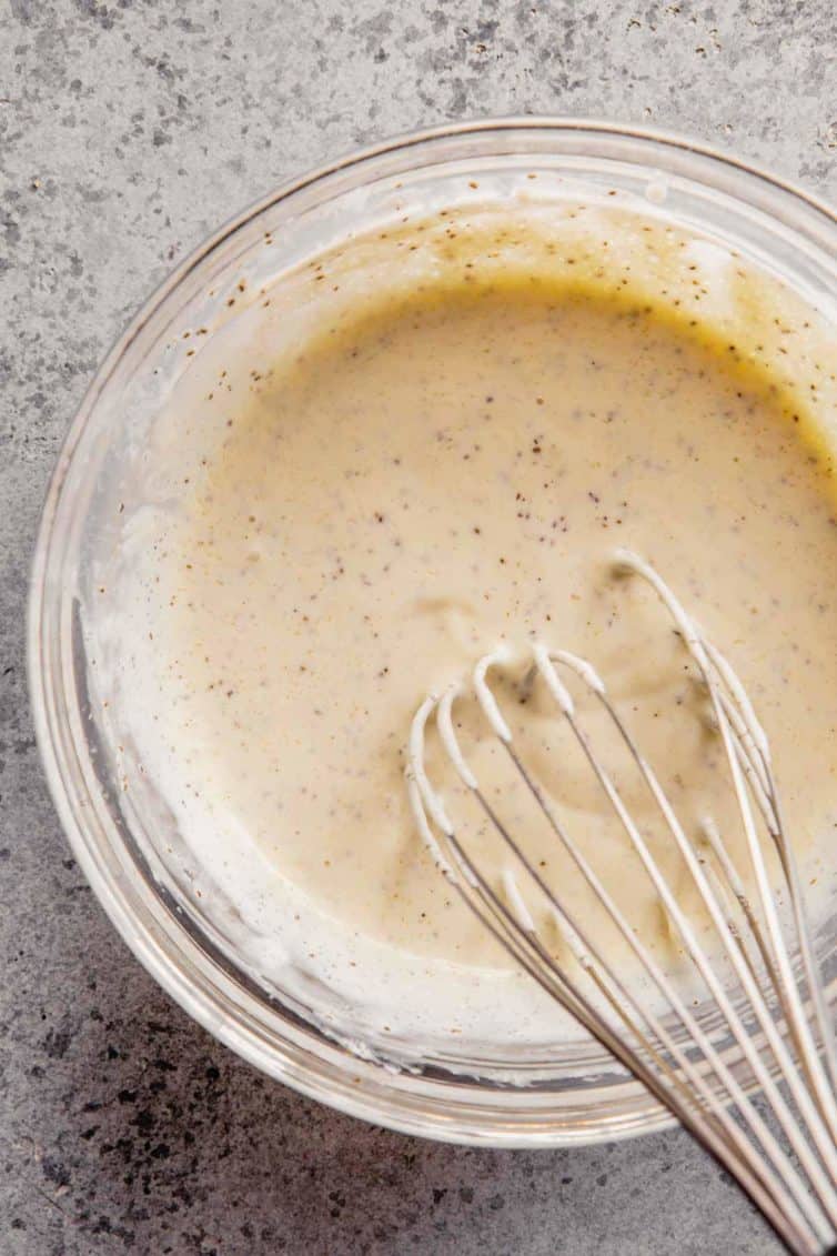 Glass bowl on the counter with a whisk with the coleslaw dressing after mixing.