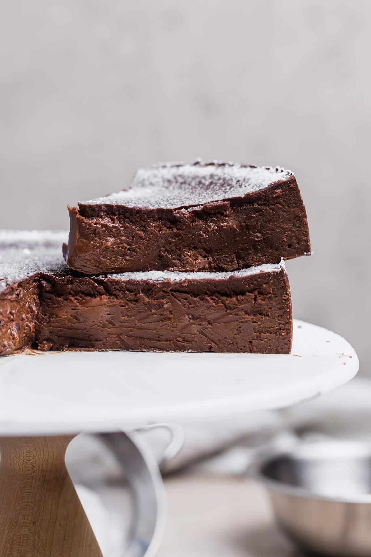 A slice of flourless chocolate cake on top of the chocolate cake on a white cake stand.