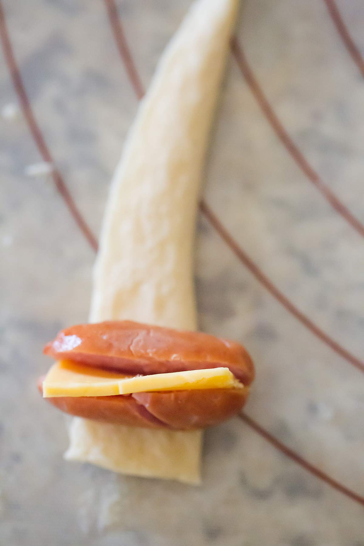 Mini hot dog with cheese stuffed inside sitting on strip of crescent roll dough.