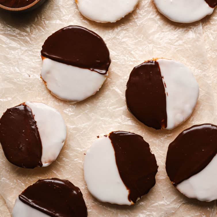 A square photo of black and white cookies on a counter covered in parchment paper.