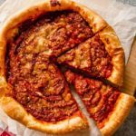 A close up of a deep-dish pizza with two slices cut out on a piece of parchment paper.