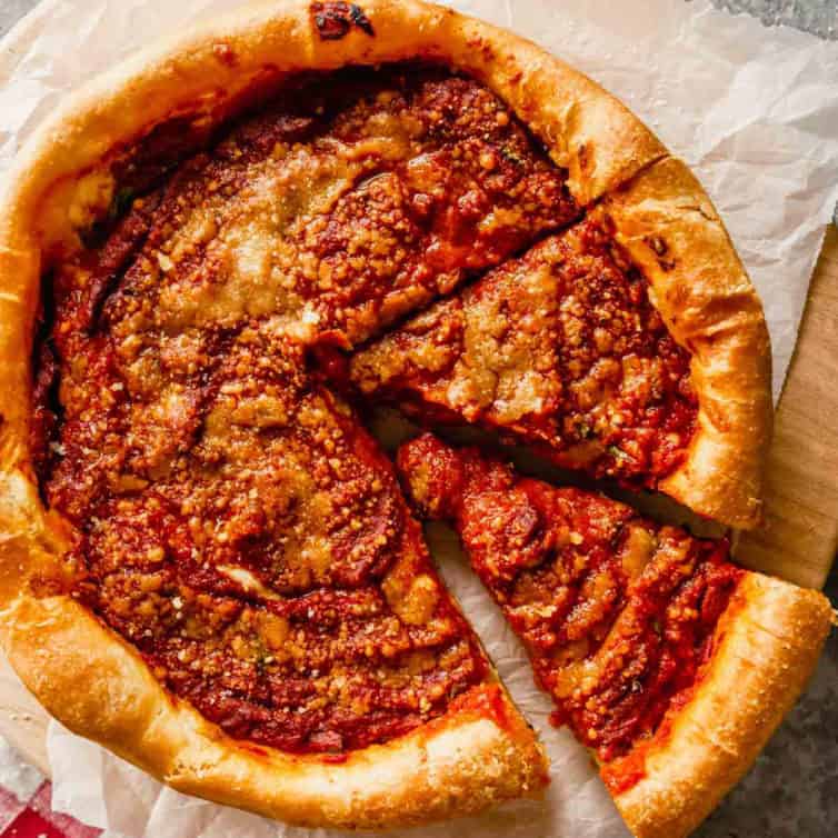 A close up of a deep-dish pizza with two slices cut out on a piece of parchment paper.