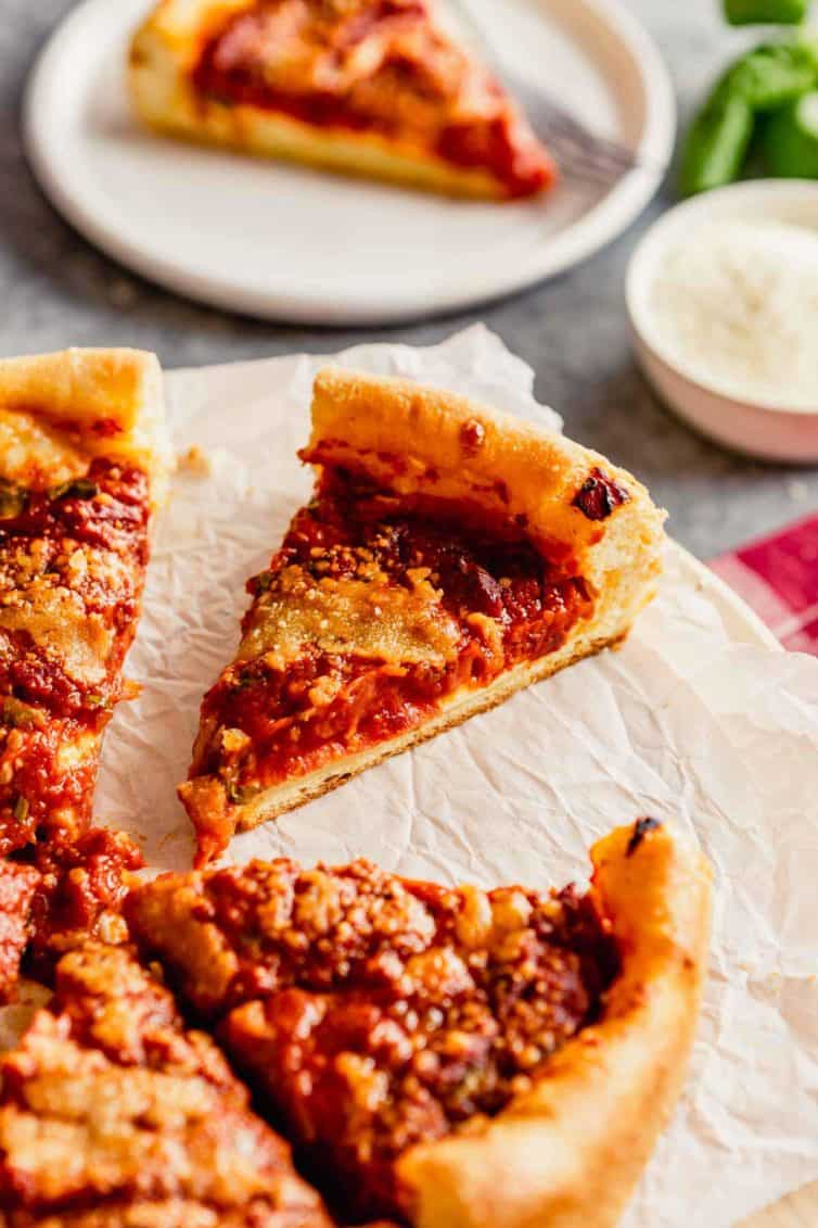 A deep dish pizza on parchment paper with a slice pulled out in the back.