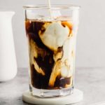 A glass of iced coffee with milk before stirring on a coaster.