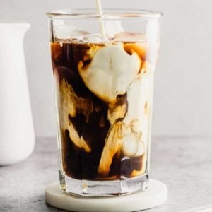 A glass of iced coffee with milk before stirring on a coaster.