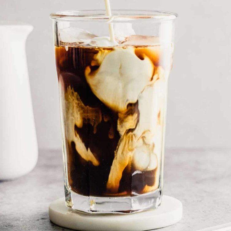 A glass of iced coffee with milk before stirring on a coaster.