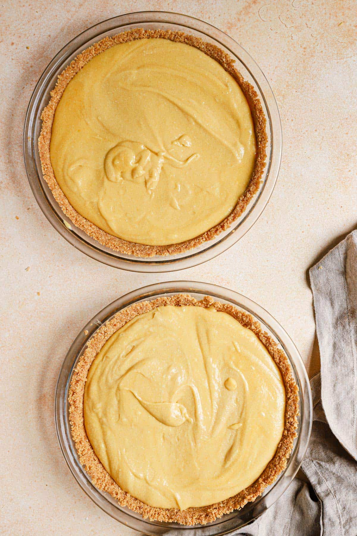 Two milk bar pies before baking on a peach colored counter with a dish towel to the bottom right.