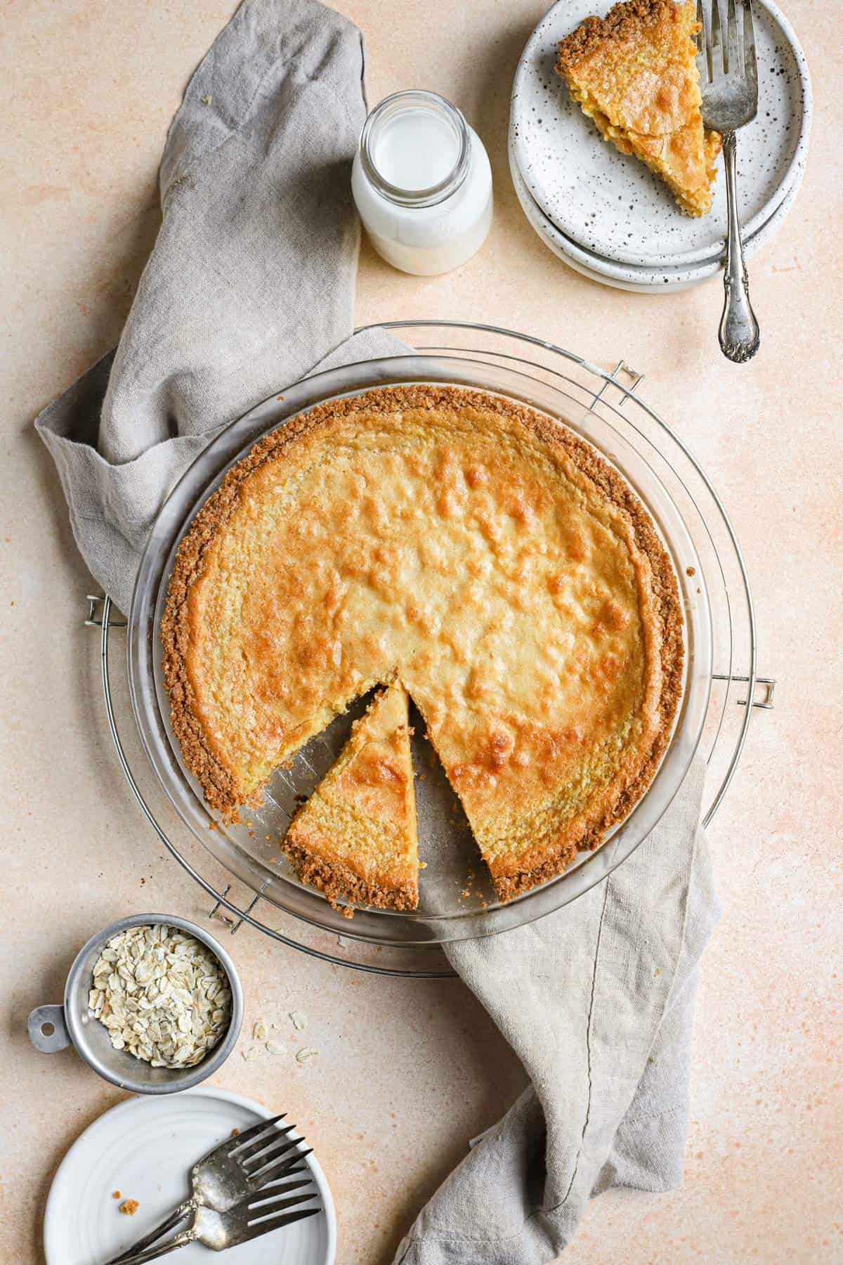 Crack pie on a round cooling rack with a slice on a plate in the top right and a slice cut out in the pie plate with a towel under the pie pan.