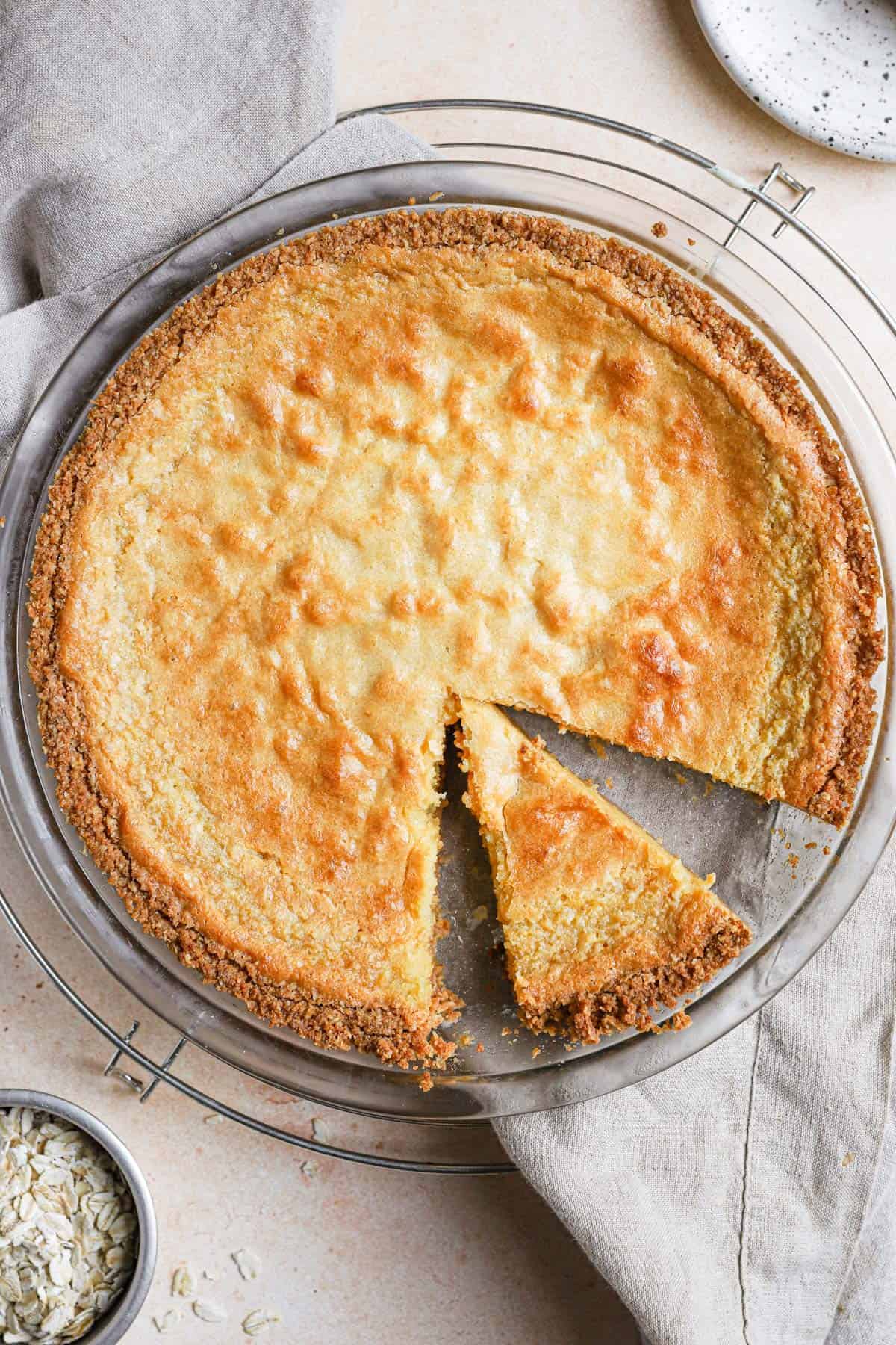 A momofuku crack pie in a pie pan on a cooling rack with a slice cut in the right bottom side of the pie.