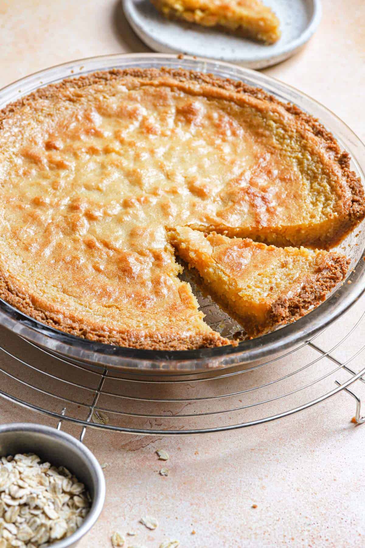 From the side, a crack pie on a cooling rack with a slice cut into the right side and a slice on a plate in the back.