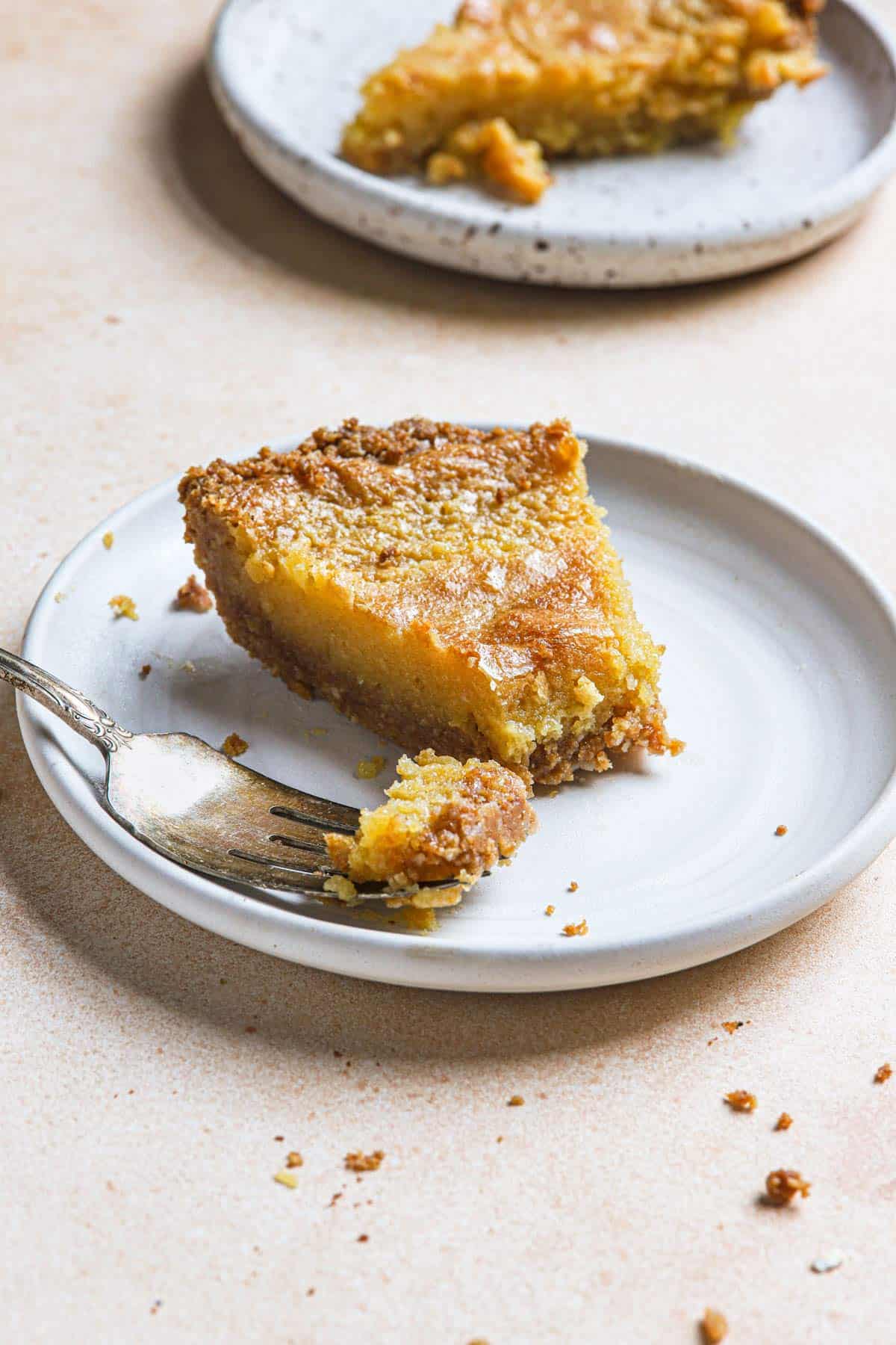 A slice of crack pie on a white plate with a bite taken out with a fork to the left.