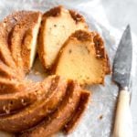 A sliced rum cake on parchment paper with a knife to the right of the cake.