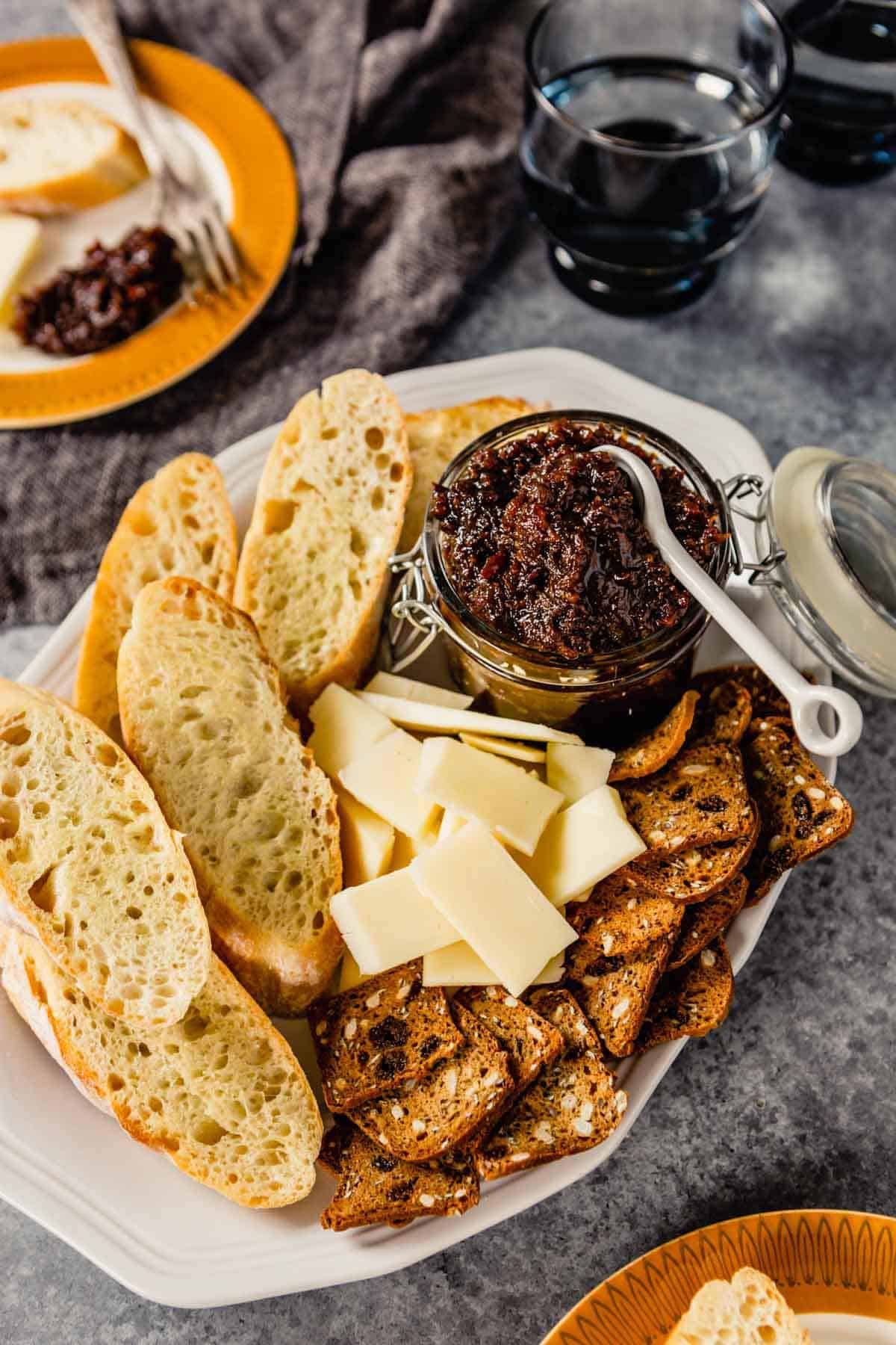 A platter with a jar of bacon jam in the top right and cheese, crackers, and bread on the platter.
