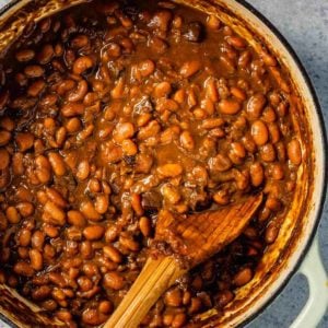 A top down photo of Boston baked beans in a dutch oven with a wooden spoon.