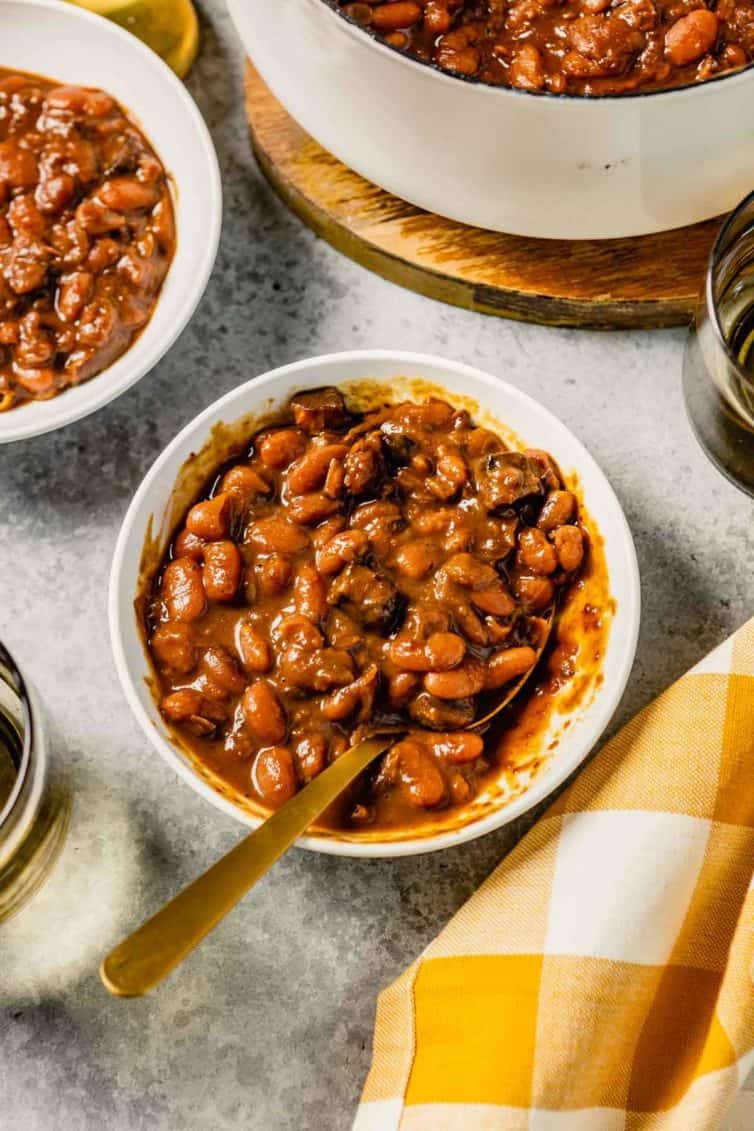 A white bowl with baked beans and a yellow and white buffalo check towel to the bottom left.