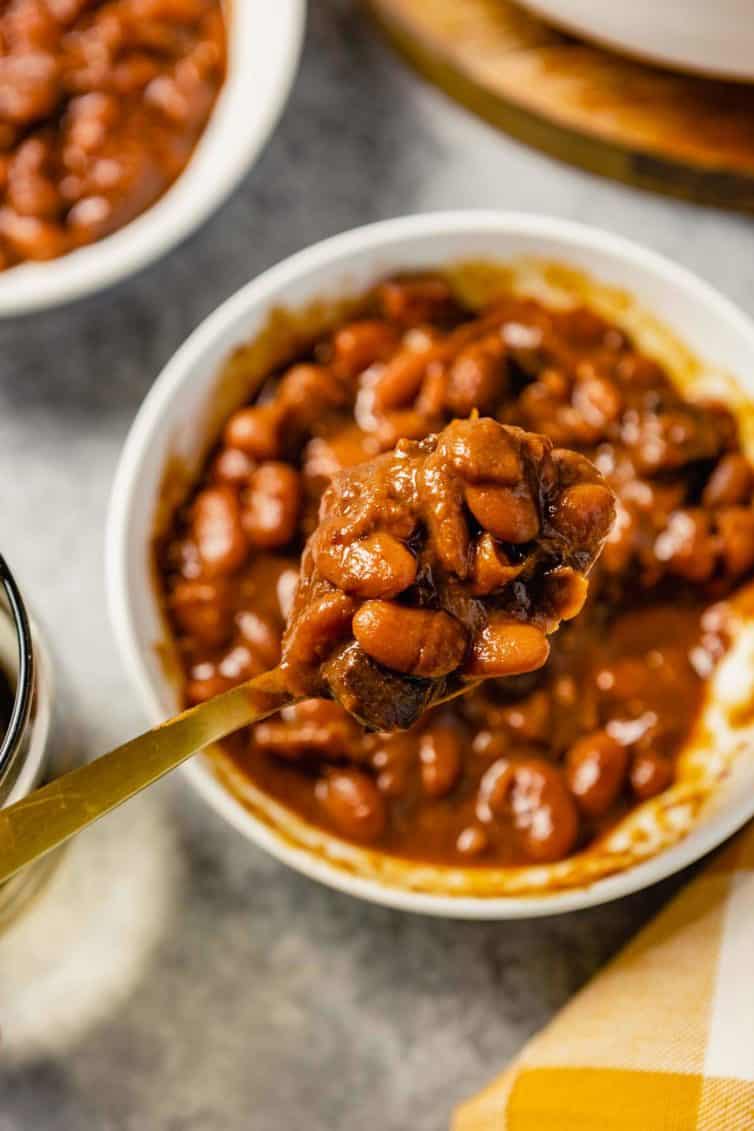 A spoon with a scoop of Boston baked beans over a white bowl.