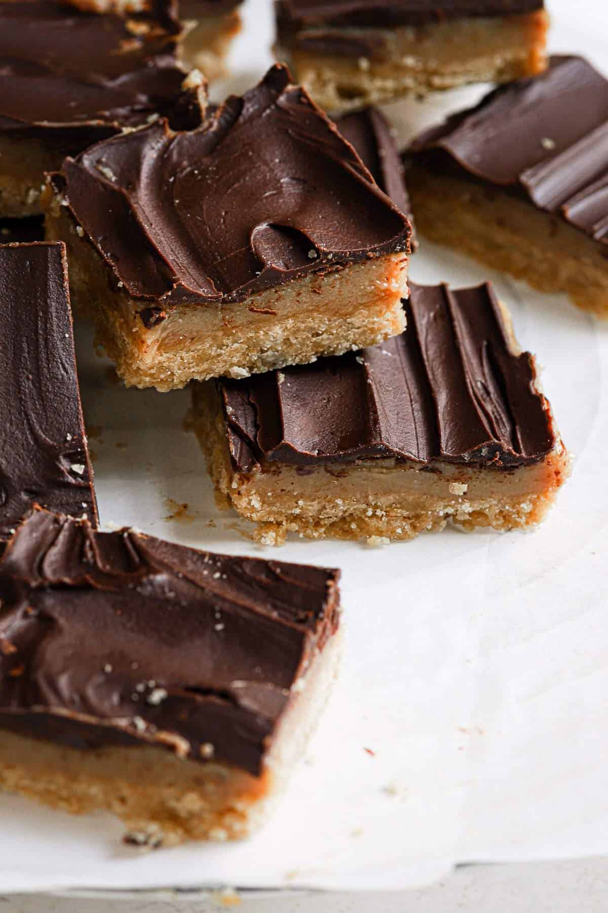 Millionaire bars cut into squares on parchment paper with one stacked on another in the front.