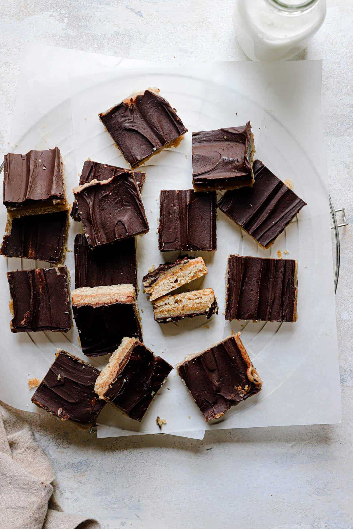 Top down photo of shortbread bars on a cooling rack topped with parchment paper and a glass of milk in the top right corner.