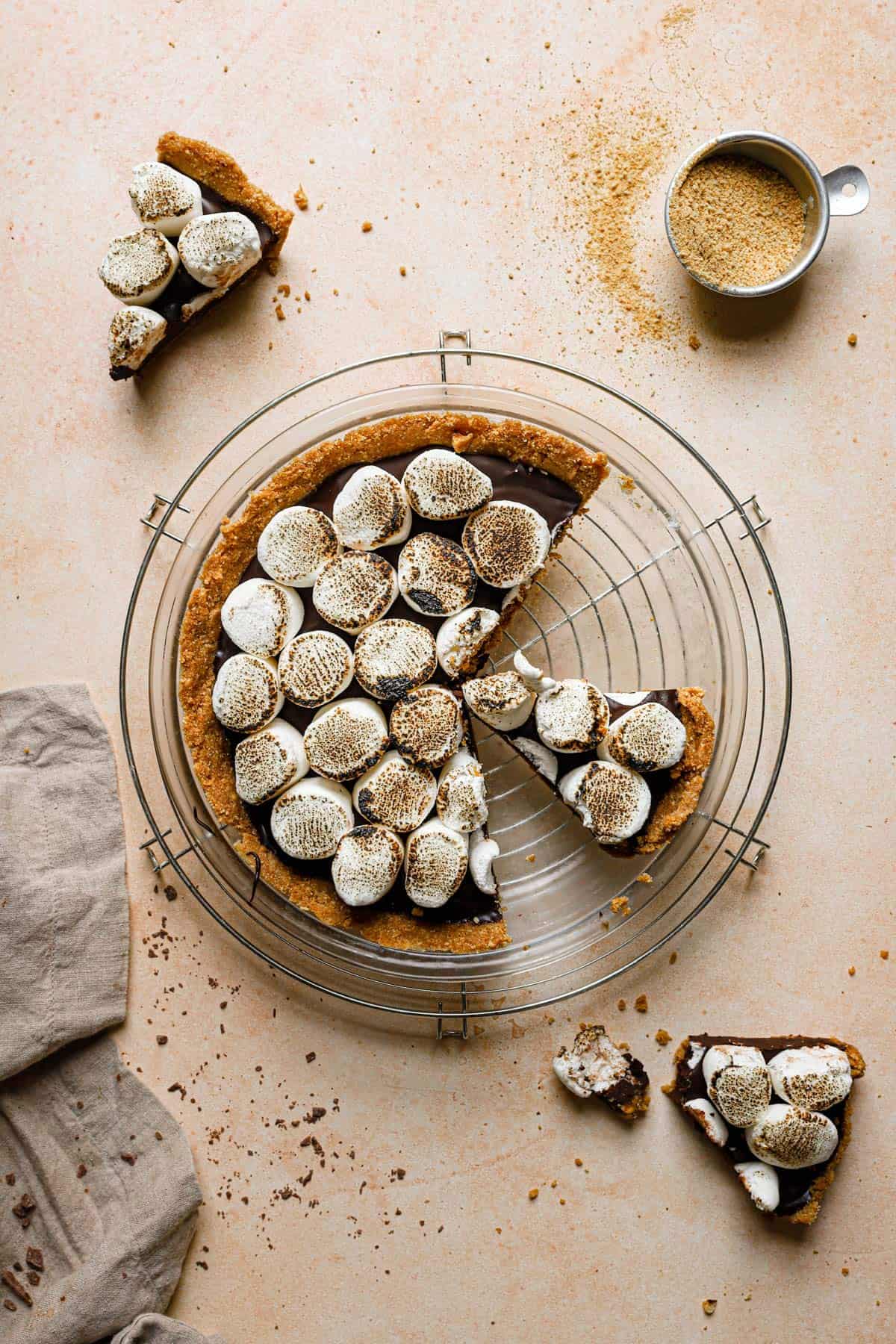 No bake s'mores pie on a wire cooling rack with a slice on the counter in the top left and bottom right.